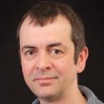 A photo of Prof Chris Metcalfe. A man with short dark hair against a black background. 